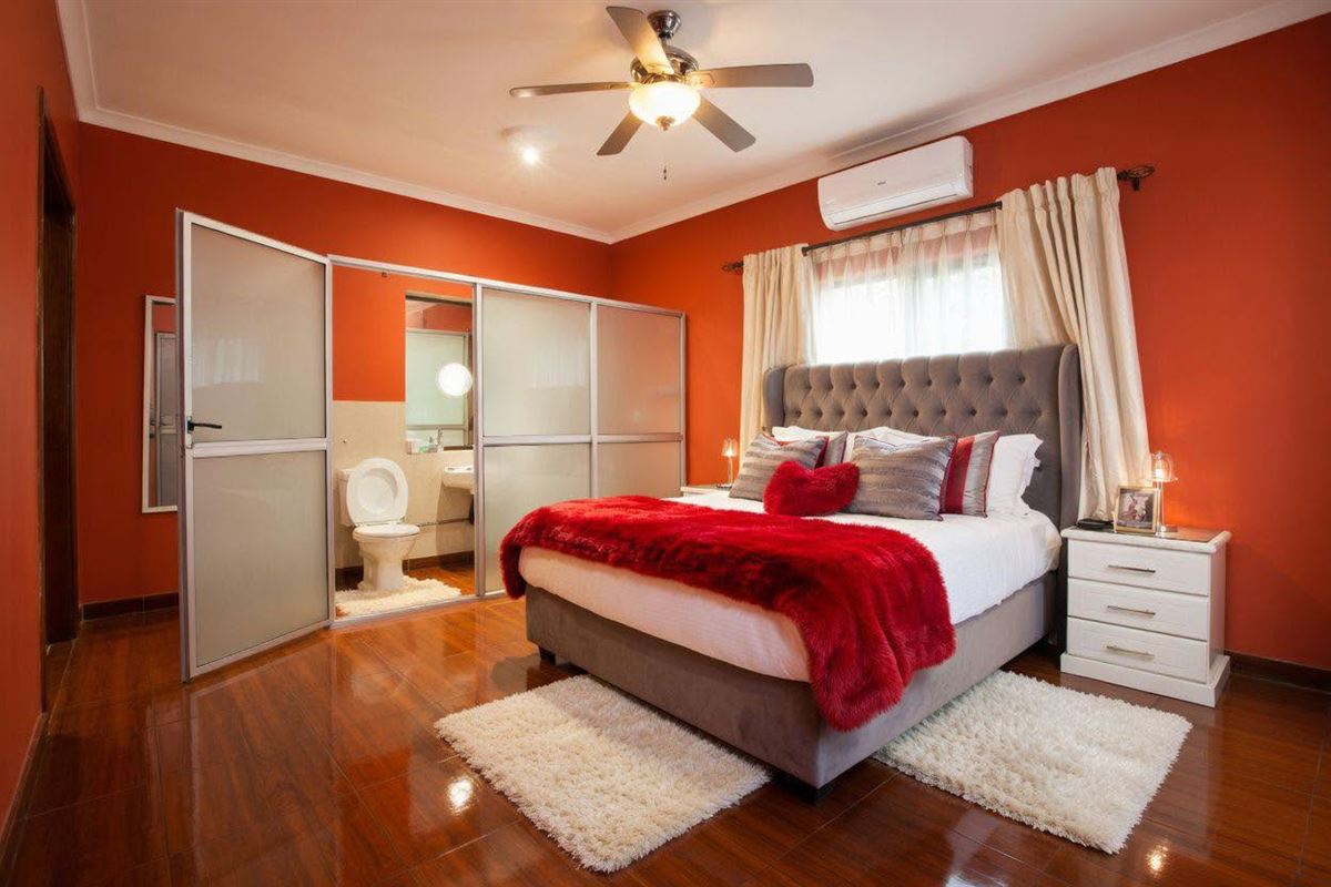 Bedroom with terracotta walls, a grey tufted headboard, a red throw and an en-suite behind frosted glass doors
