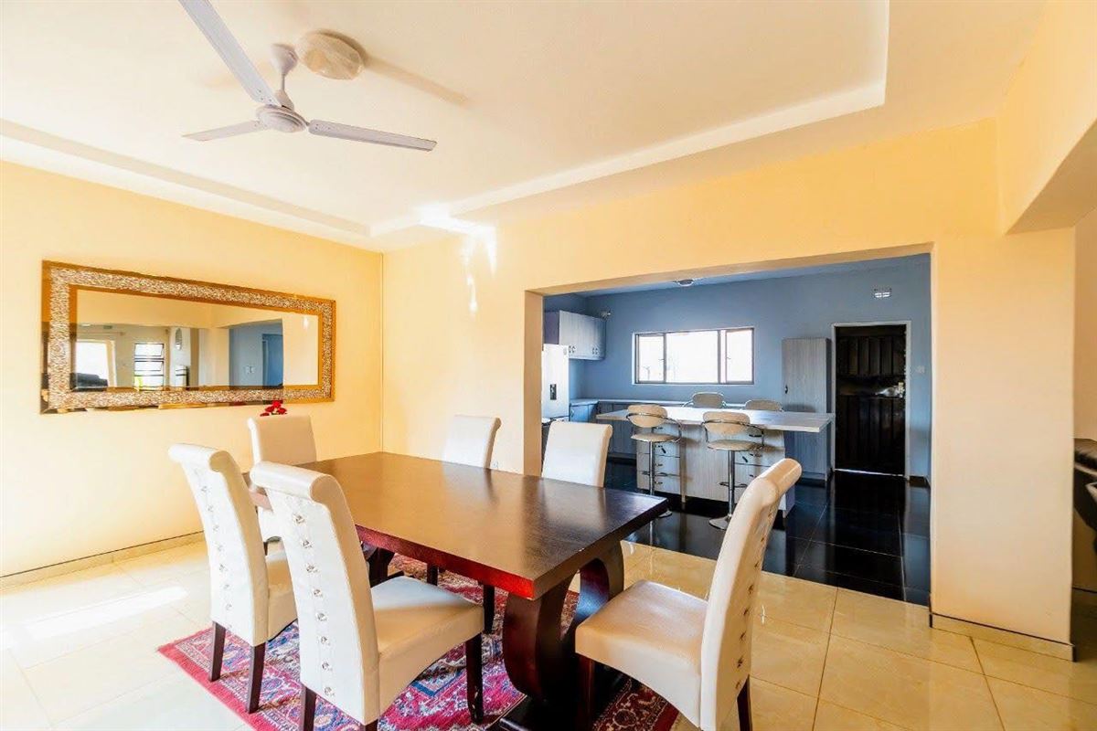 Dining table with white chairs on a patterned rug, open to a kitchen with a breakfast bar